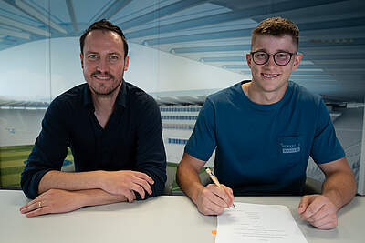 Max Weiß und Sebastian Freis sitzen am Tisch und grinsen in die Kamera.